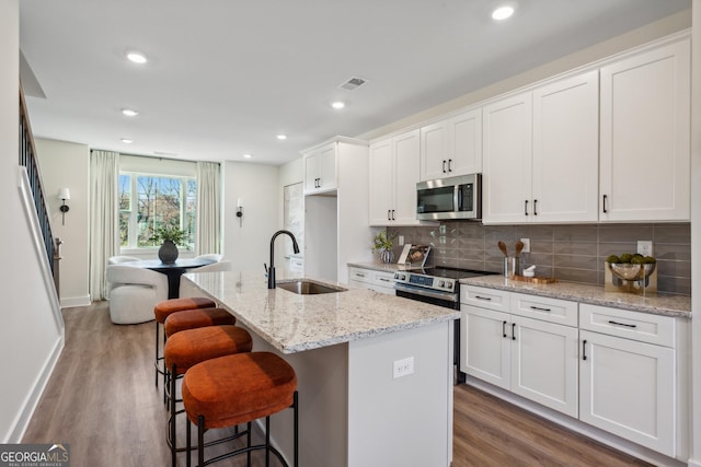 kitchen with sink, white cabinets, stainless steel appliances, and a center island with sink