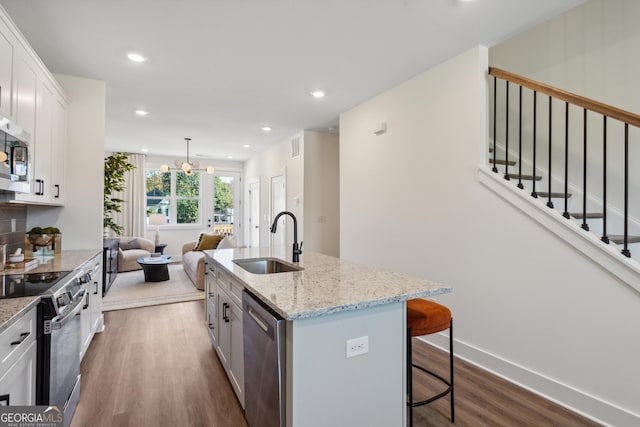 kitchen featuring a kitchen island with sink, white cabinets, sink, a notable chandelier, and stainless steel appliances