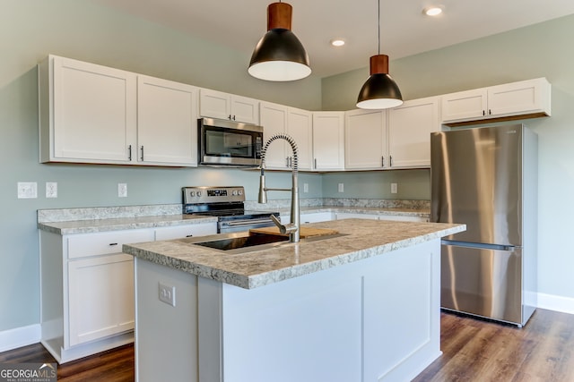 kitchen featuring appliances with stainless steel finishes, a kitchen island with sink, dark wood-type flooring, decorative light fixtures, and white cabinets