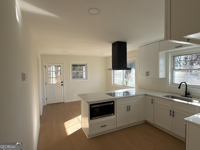 kitchen featuring built in microwave, sink, island exhaust hood, kitchen peninsula, and white cabinets