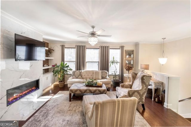 living room featuring hardwood / wood-style flooring, ceiling fan, a premium fireplace, and crown molding