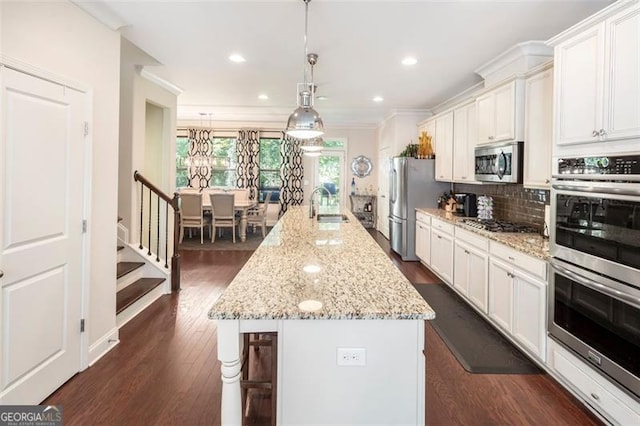 kitchen featuring sink, stainless steel appliances, a large island with sink, decorative backsplash, and white cabinets