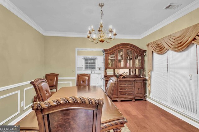 dining area with light hardwood / wood-style floors, sink, ornamental molding, and a notable chandelier