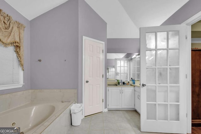 bathroom with tile patterned floors, vanity, a relaxing tiled tub, and vaulted ceiling