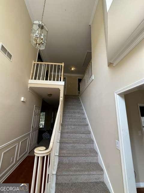 stairs with a towering ceiling, an inviting chandelier, and ornamental molding