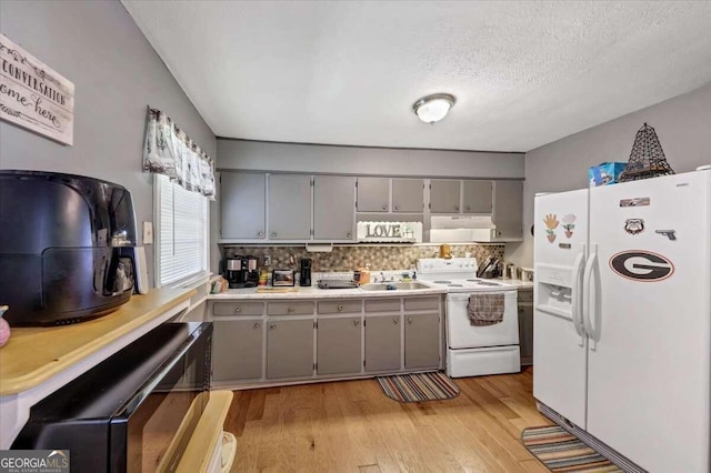 kitchen with gray cabinetry, stove, white fridge with ice dispenser, and sink