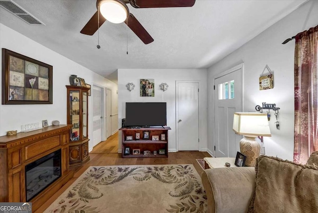 living room with hardwood / wood-style flooring, ceiling fan, and a textured ceiling