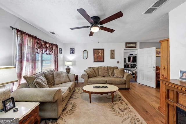 living room featuring ceiling fan, a textured ceiling, and light hardwood / wood-style flooring