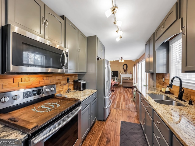 kitchen with hardwood / wood-style floors, backsplash, sink, light stone counters, and stainless steel appliances