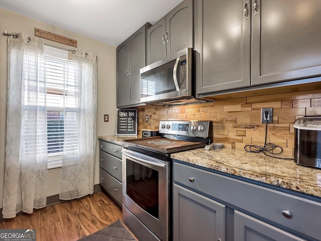 kitchen featuring light stone counters, dark hardwood / wood-style floors, gray cabinets, decorative backsplash, and appliances with stainless steel finishes