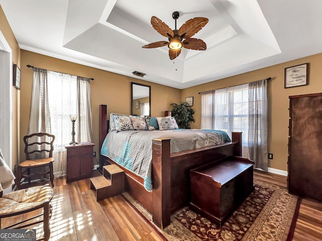 bedroom with wood-type flooring, a tray ceiling, and ceiling fan