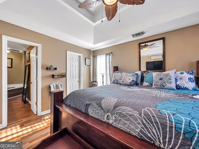 bedroom with hardwood / wood-style floors, ceiling fan, and a tray ceiling