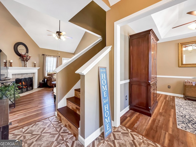 stairs with wood-type flooring, ceiling fan, and a tiled fireplace