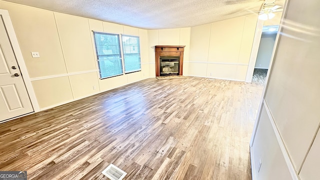 unfurnished living room with ceiling fan, light hardwood / wood-style floors, and a textured ceiling