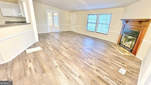 unfurnished living room with french doors, a textured ceiling, light hardwood / wood-style floors, and vaulted ceiling