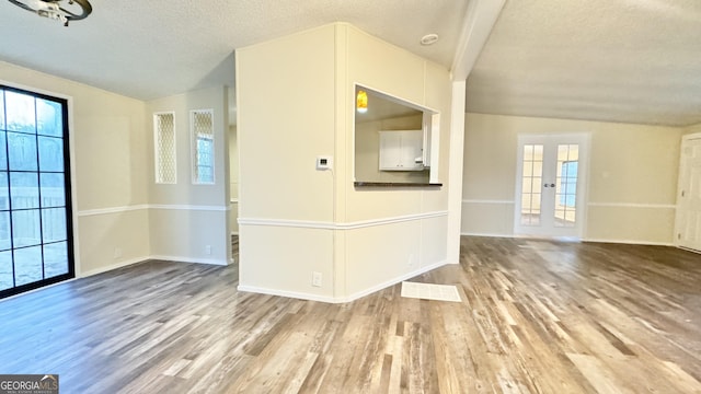 unfurnished living room with hardwood / wood-style floors, lofted ceiling, a textured ceiling, and french doors