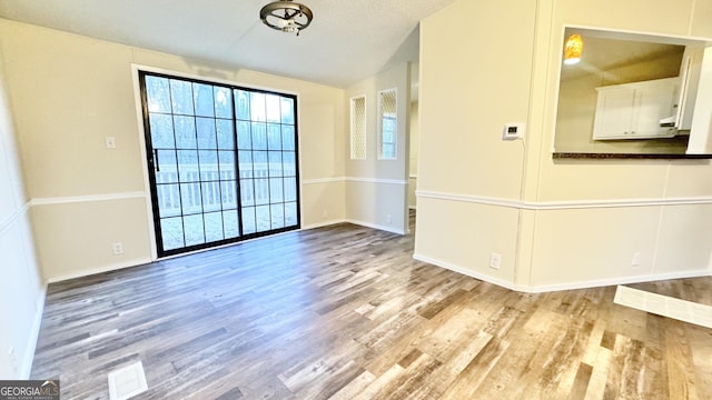 unfurnished room with a textured ceiling, light hardwood / wood-style flooring, and lofted ceiling