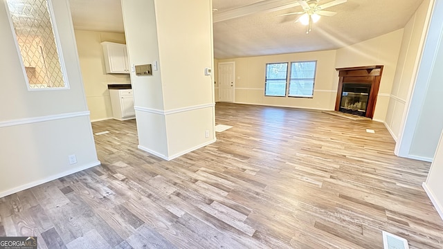 unfurnished living room featuring a textured ceiling, light hardwood / wood-style flooring, ceiling fan, and vaulted ceiling