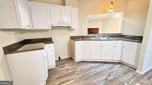 kitchen with pendant lighting, white cabinets, sink, dark stone countertops, and light wood-type flooring