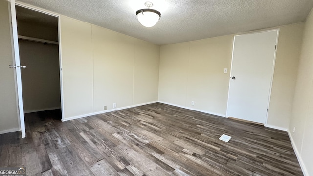 unfurnished bedroom featuring a textured ceiling, a walk in closet, dark hardwood / wood-style flooring, and a closet