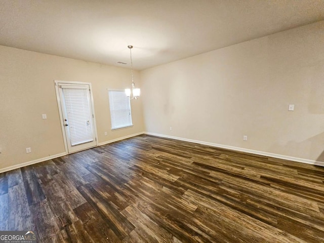 unfurnished room featuring dark wood-type flooring and a notable chandelier