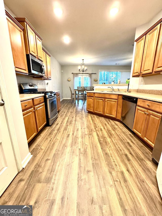 kitchen featuring pendant lighting, an inviting chandelier, light hardwood / wood-style flooring, appliances with stainless steel finishes, and kitchen peninsula