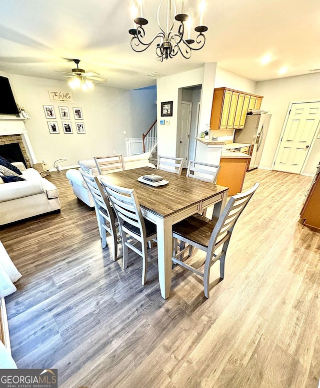 dining room with a stone fireplace, light hardwood / wood-style floors, and ceiling fan with notable chandelier