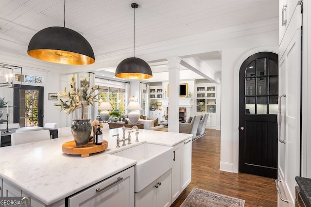 kitchen with pendant lighting, white cabinets, a brick fireplace, light stone counters, and a center island with sink