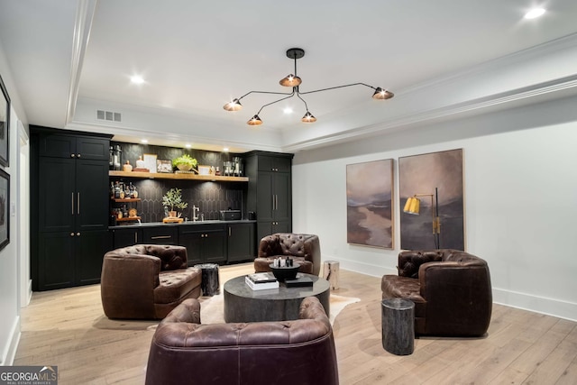 living room featuring light hardwood / wood-style floors, bar area, a tray ceiling, and ornamental molding