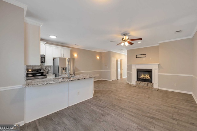 kitchen featuring kitchen peninsula, light stone countertops, white cabinetry, wood-type flooring, and stainless steel appliances