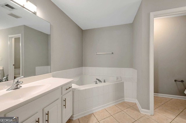 bathroom with tile patterned flooring, vanity, toilet, and tiled bath