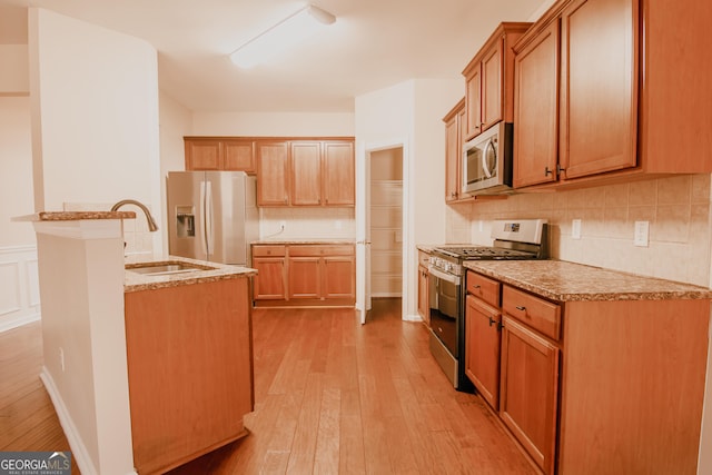 kitchen with appliances with stainless steel finishes, an island with sink, sink, backsplash, and light hardwood / wood-style flooring