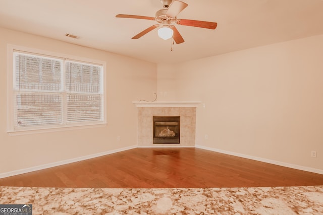 unfurnished living room featuring ceiling fan, hardwood / wood-style floors, and a tile fireplace