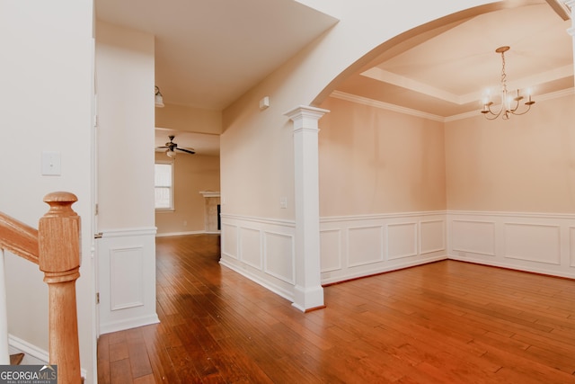 spare room featuring decorative columns, ornamental molding, a raised ceiling, hardwood / wood-style flooring, and ceiling fan with notable chandelier