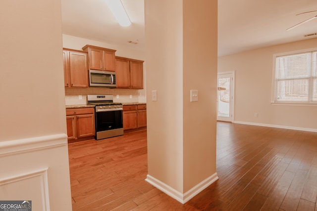 kitchen featuring tasteful backsplash, light stone counters, stainless steel appliances, and light wood-type flooring