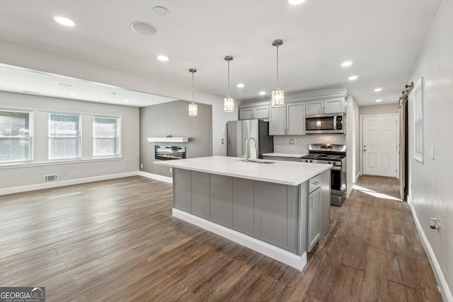 kitchen featuring a barn door, stainless steel appliances, a center island with sink, and gray cabinetry