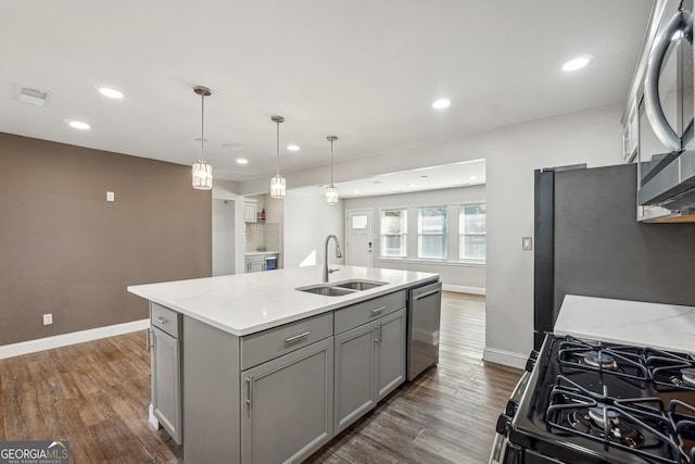 kitchen with appliances with stainless steel finishes, light stone counters, gray cabinetry, sink, and an island with sink