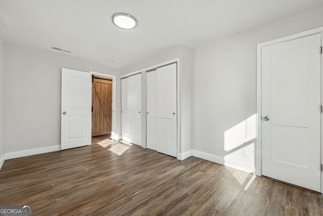 unfurnished bedroom featuring a barn door and dark hardwood / wood-style flooring