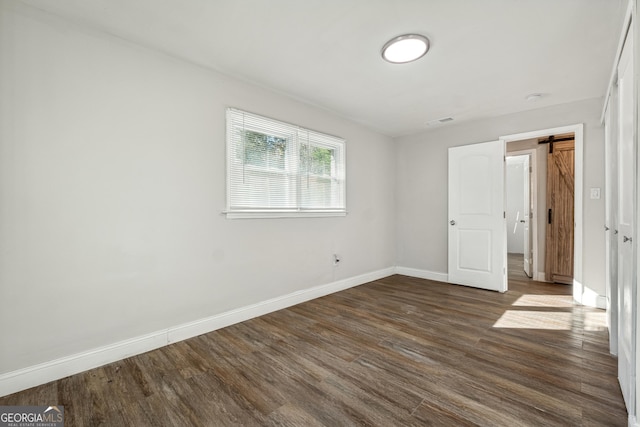 unfurnished bedroom featuring dark hardwood / wood-style floors and a barn door