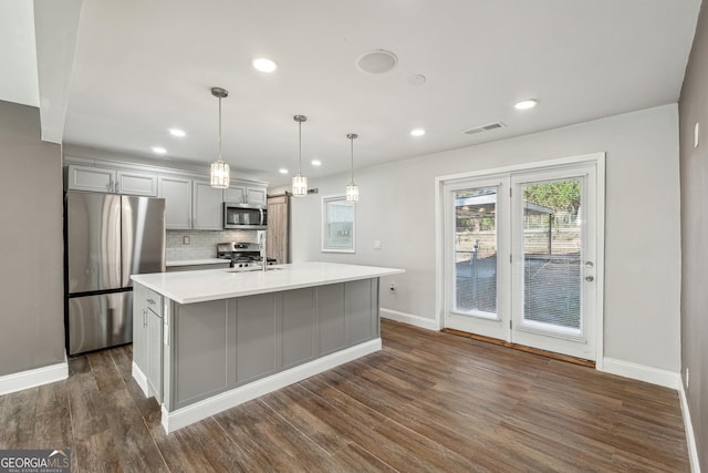 kitchen featuring gray cabinetry, backsplash, a kitchen island with sink, decorative light fixtures, and stainless steel appliances