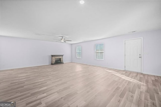 unfurnished living room with light hardwood / wood-style floors, a stone fireplace, and ceiling fan