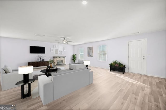 living room with ceiling fan, a stone fireplace, and light wood-type flooring