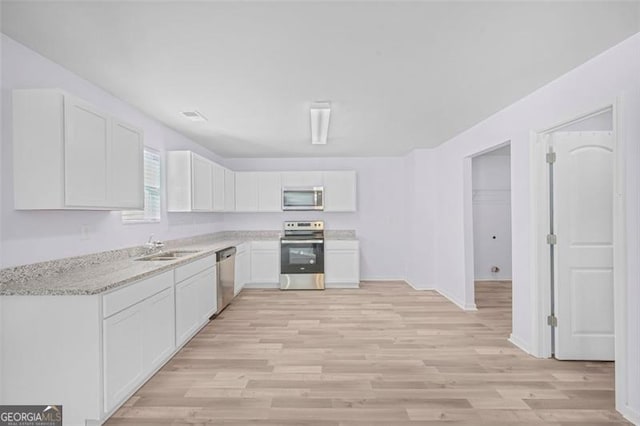 kitchen featuring light stone countertops, light wood-type flooring, stainless steel appliances, sink, and white cabinets