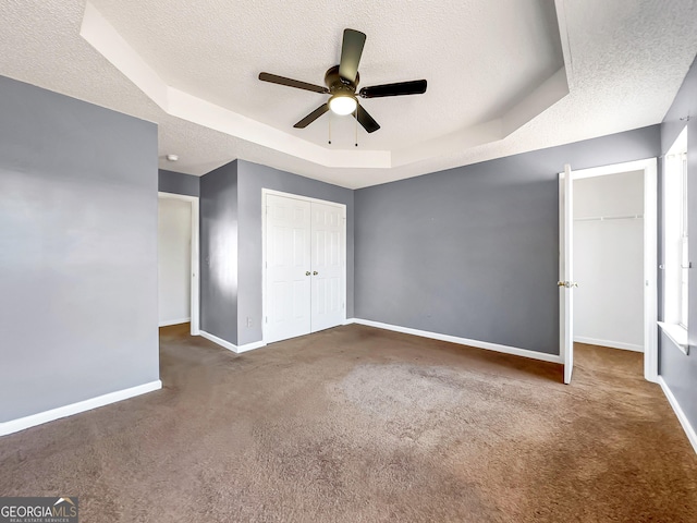 unfurnished bedroom with dark colored carpet, ceiling fan, a tray ceiling, a textured ceiling, and a closet