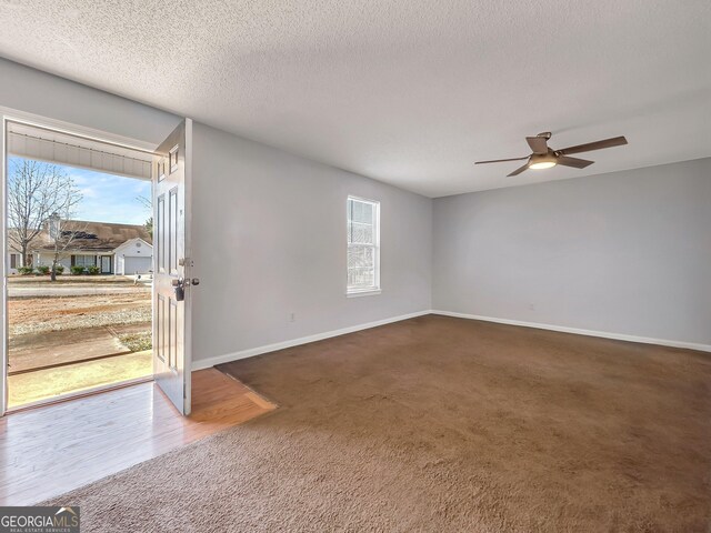 empty room with a textured ceiling, dark carpet, and ceiling fan