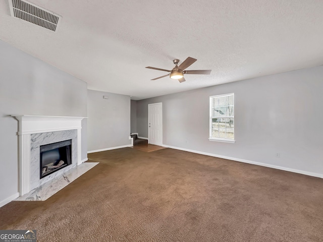 unfurnished living room featuring a textured ceiling, ceiling fan, dark carpet, and a fireplace