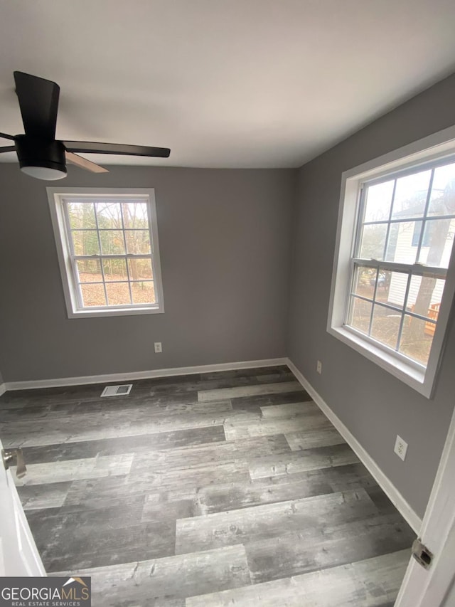 unfurnished room featuring plenty of natural light, ceiling fan, and dark hardwood / wood-style flooring