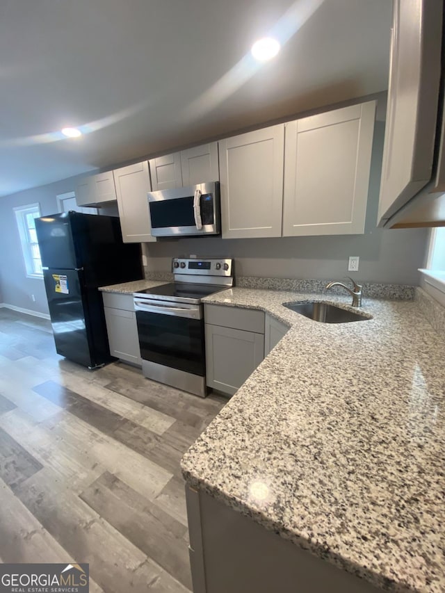 kitchen with light stone countertops, sink, light hardwood / wood-style floors, and appliances with stainless steel finishes