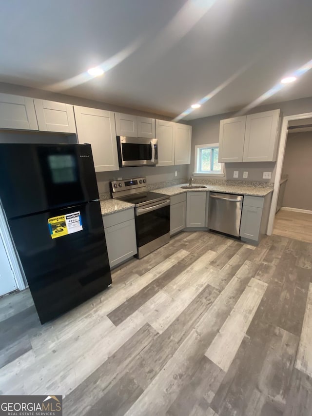 kitchen with light stone counters, sink, stainless steel appliances, and light hardwood / wood-style floors