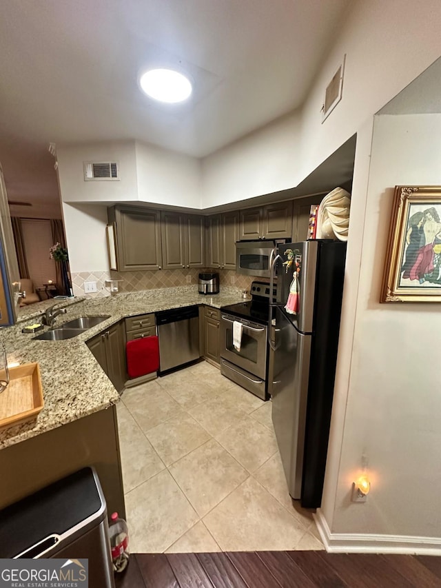 kitchen featuring sink, tasteful backsplash, light stone counters, kitchen peninsula, and appliances with stainless steel finishes